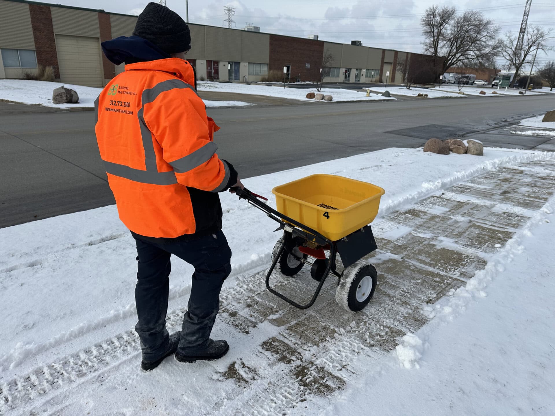 Worker with cart cleaning snow and ice from sidewalk in winter.